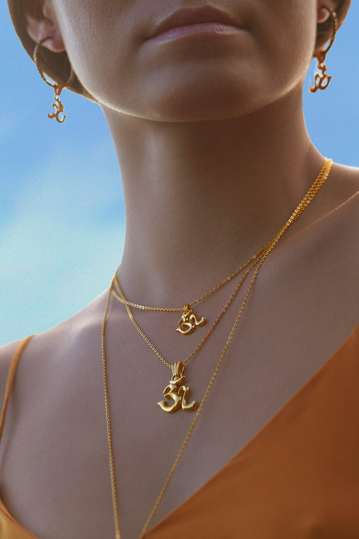 Steffi is wearing two spiritual necklaces from the Om jewelry collection, along with matching hoop earrings featuring Om symbols.