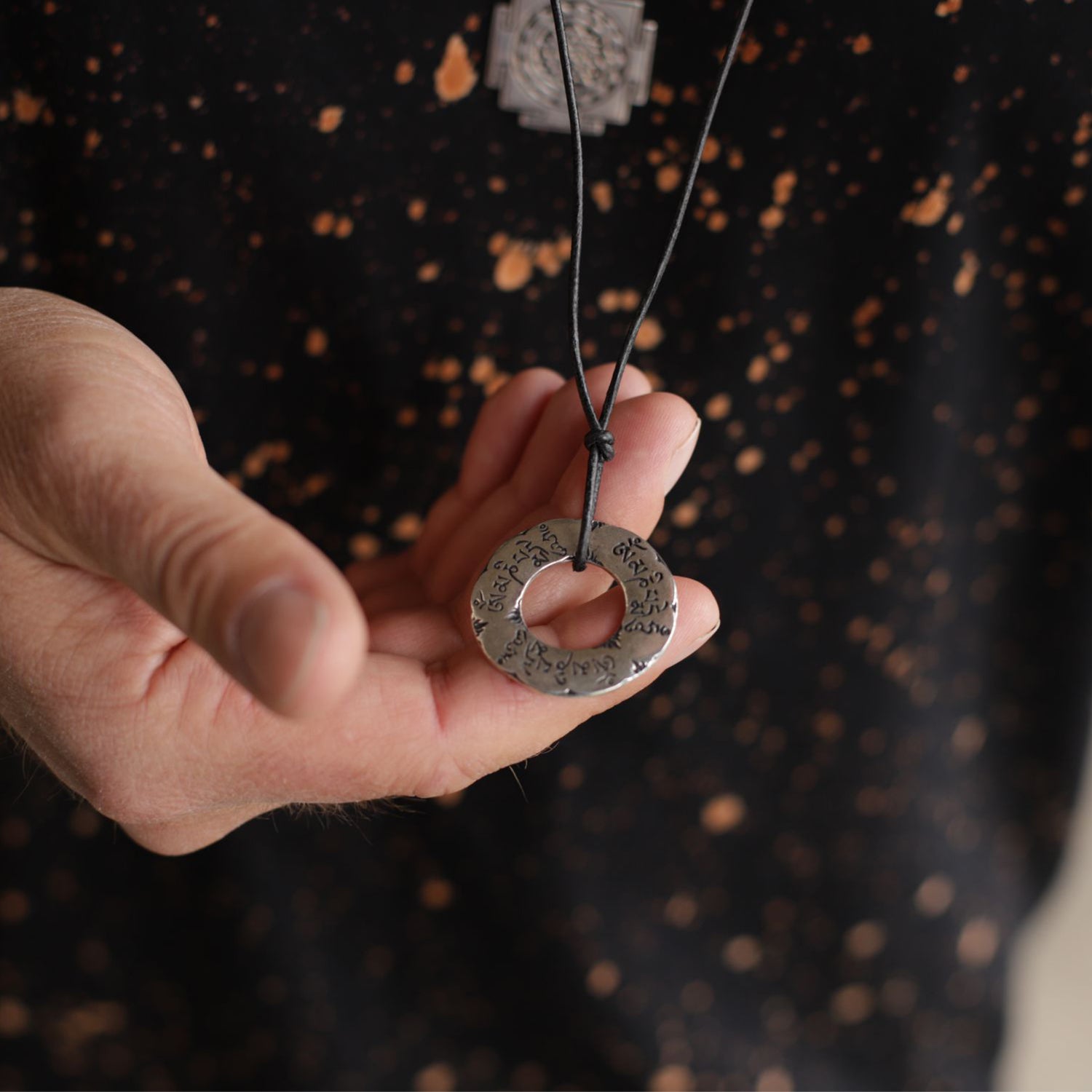 Yoga Lehrer Valentin hält ein Om Mani Padme Hum Mantra Anhänger groß Silber mit Lederband von ETERNAL BLISS in seiner Hand