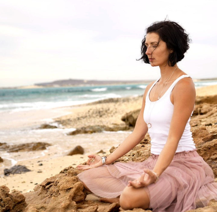 Die Yogalehrerin Beate Tschirch meditiert am Strand und trägt eine rosévergoldete Krishna Mantra Kette aus Sterling Silber von Eternal Bliss
