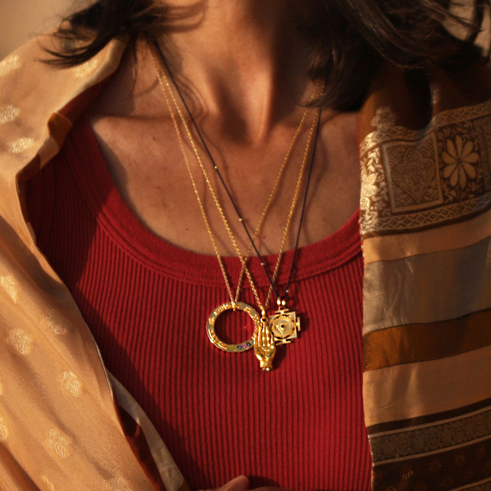 Cora trägt einen Kali Mantra Anhänger aus vergoldetem Sterling Silber mit Rubin und Saphir Edelsteinen von ETERNAL BLISS